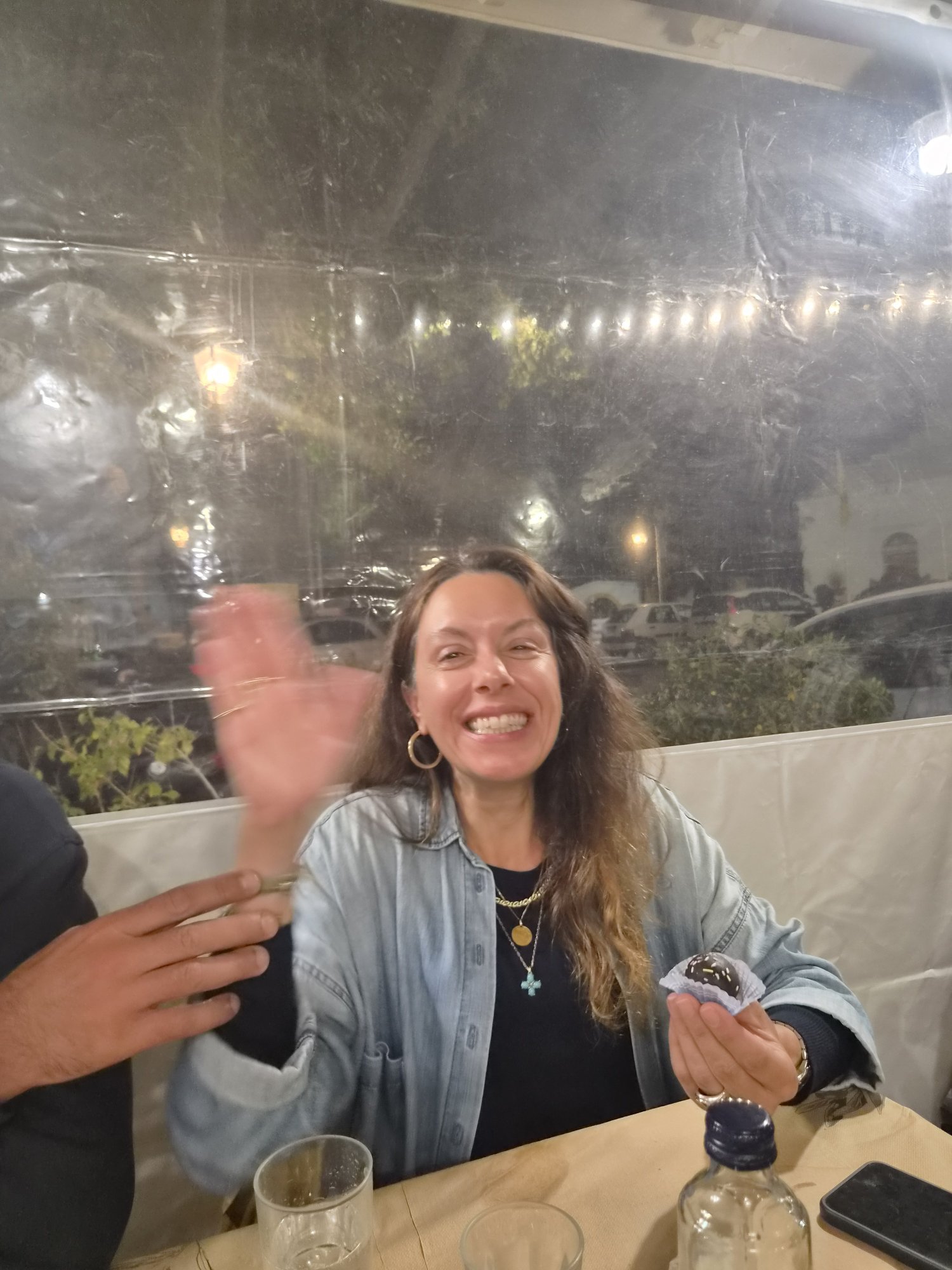 Viki laughing and waving at a restaurant table, holding a chocolate truffle